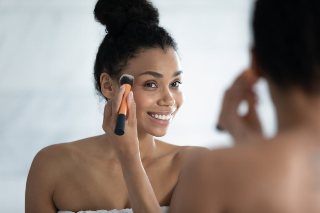 Head shot close up smiling African American young woman using cosmetics brush