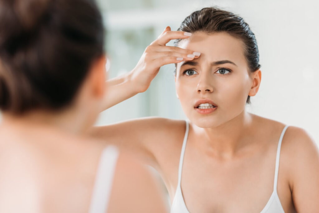 attractive young woman touching forehead and looking at mirror in bathroom