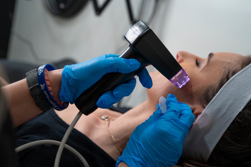 A dark-haired woman with a machine pressed near her cheek gets a Morpheus8 treatment done to enhance the appearance of her skin.