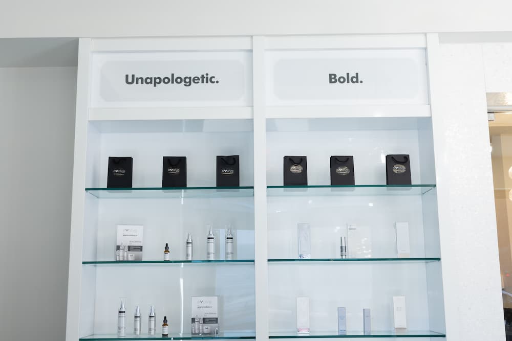 A white 3-tier shelf with various Evolve Medspa brand skincare products. This includes the Intensive Recovery Cream to use after treatments.