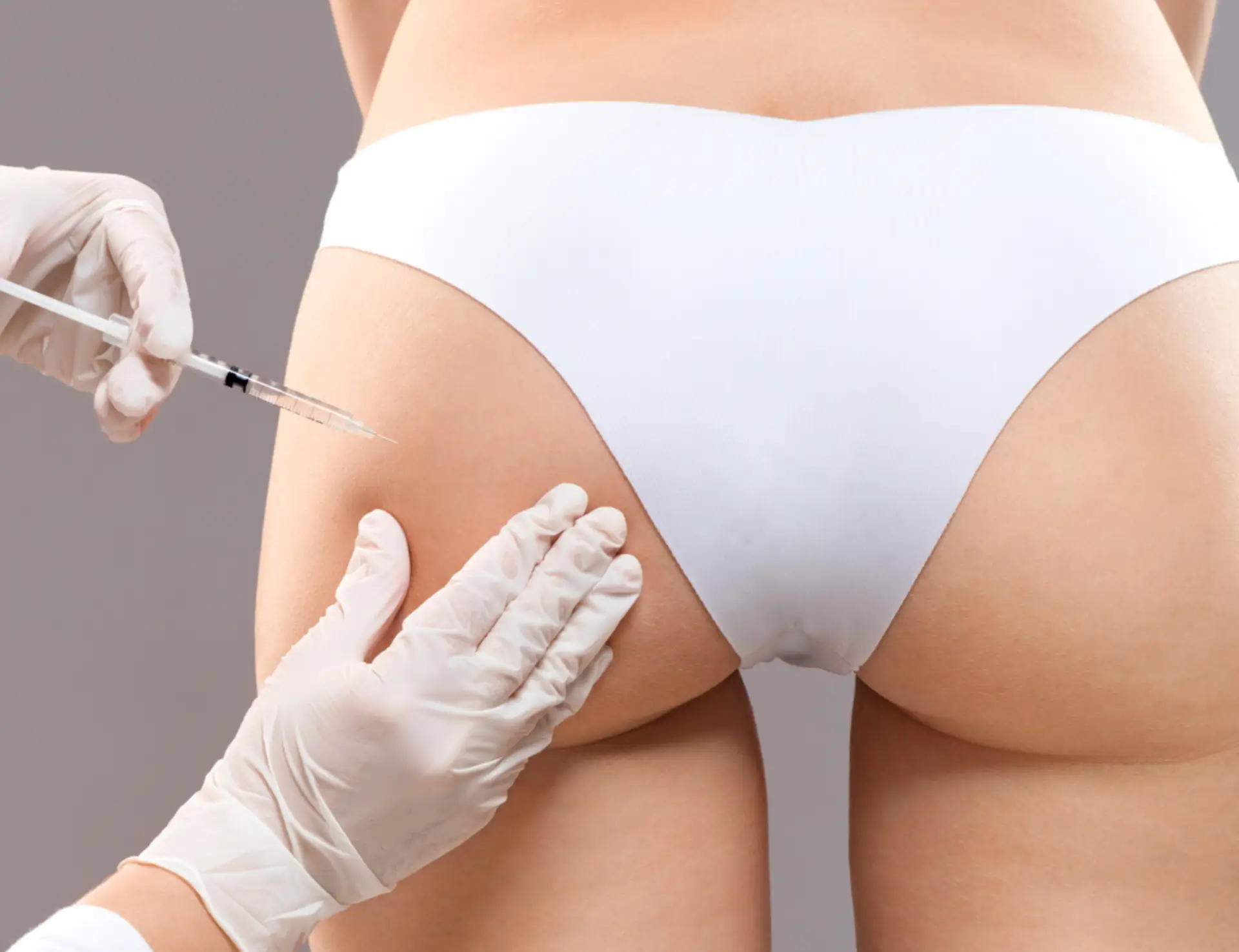 A professional performing a non-surgical butt lift procedure, injecting treatment into the patient’s gluteal area while wearing gloves, with the patient in white undergarments.