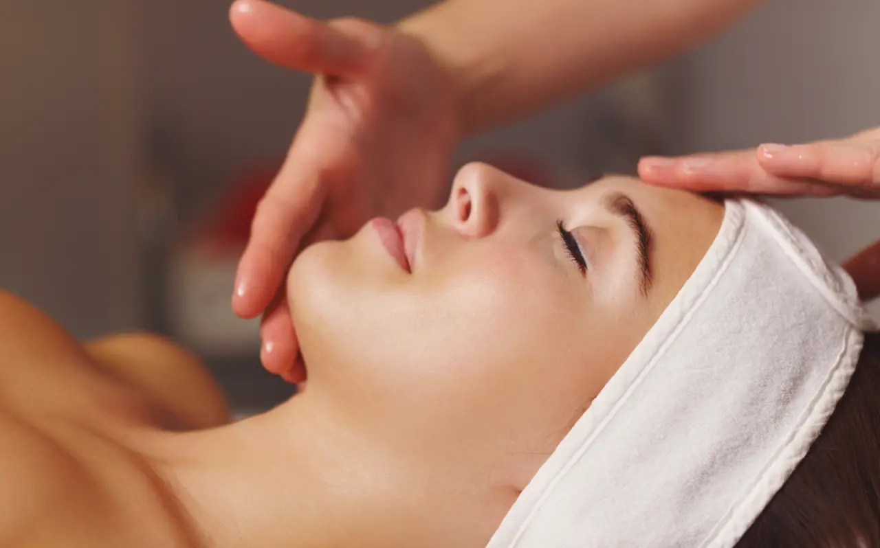 A person receiving a relaxing facial treatment at a evolve med spa, with a white headband securing their hair and hands gently massaging their forehead and face.