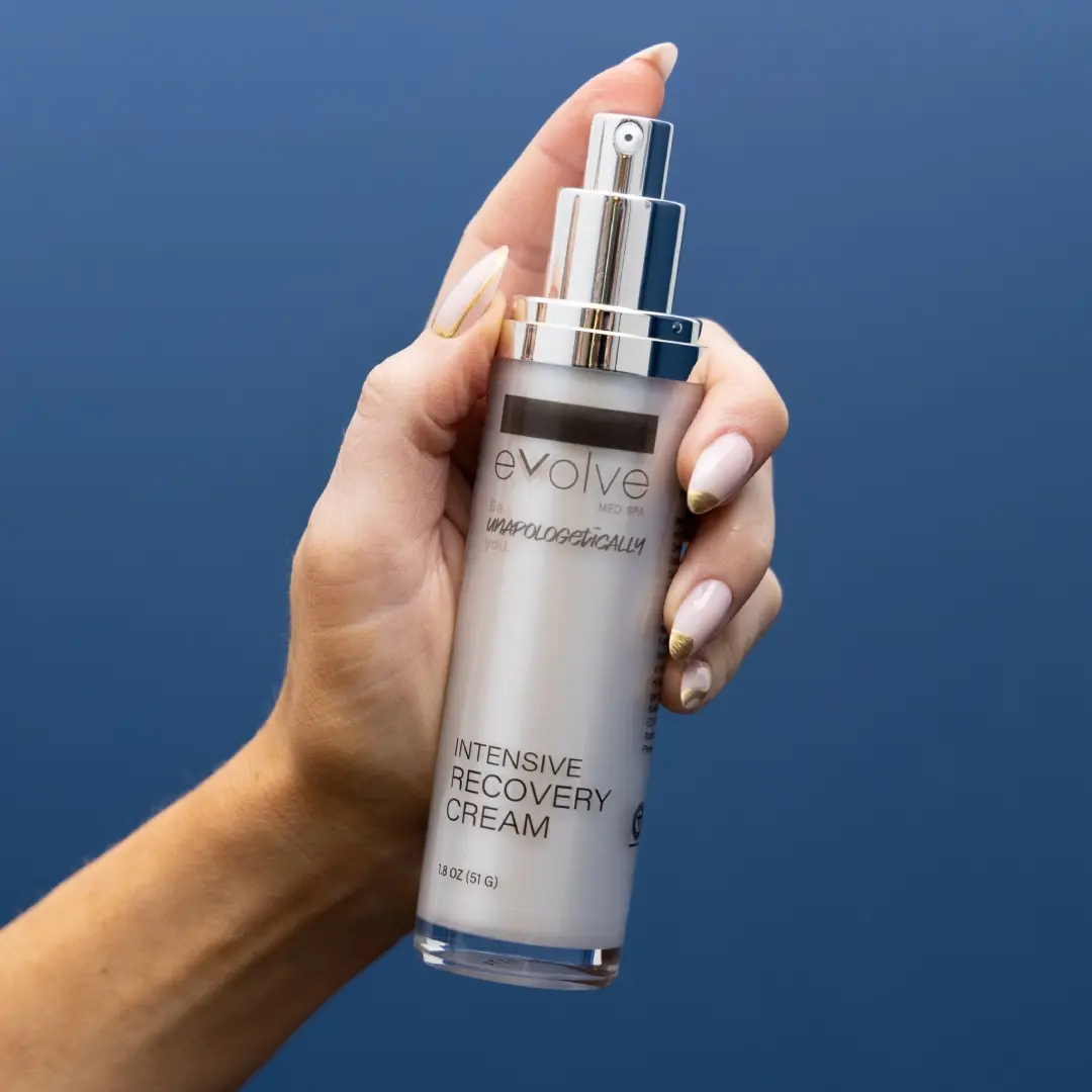 A hand holding a sleek bottle of Evolve Med Spa Intensive Recovery Cream with a silver pump dispenser