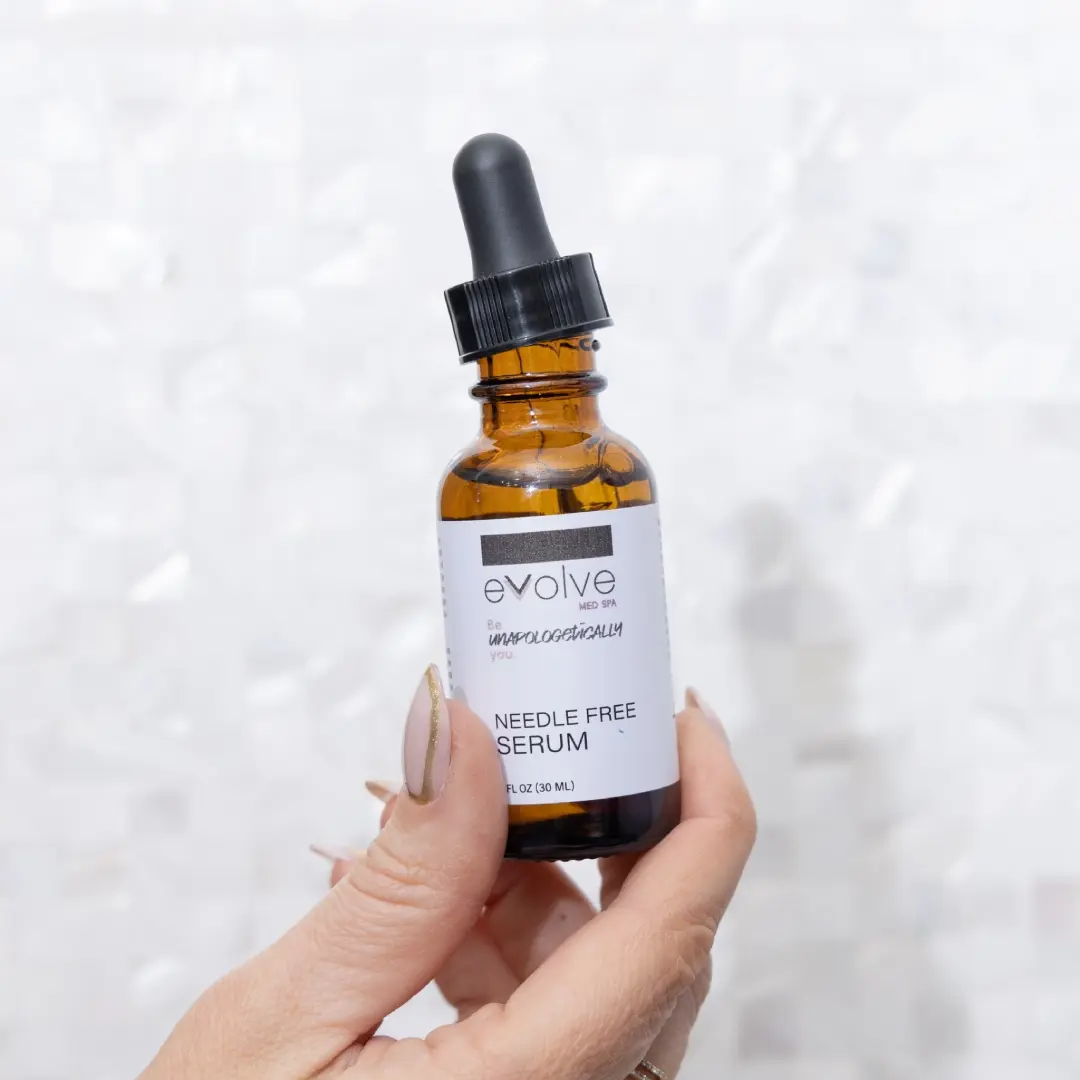 A hand holding a brown glass bottle of Evolve Med Spa Needle Free Serum