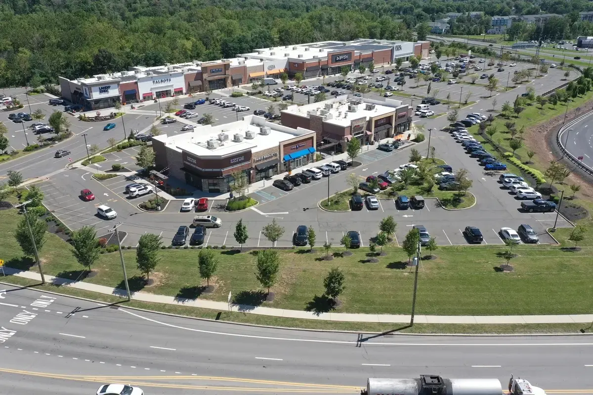 Aerial view of a shopping center with multiple stores, parking lots, and surrounding greenery.