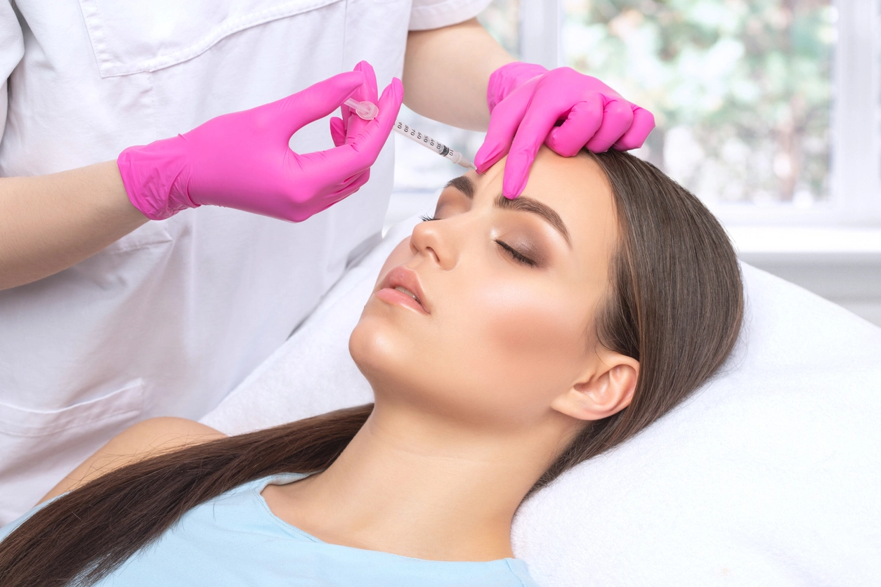 Provider injecting forehead, pink gloves, patient lying down