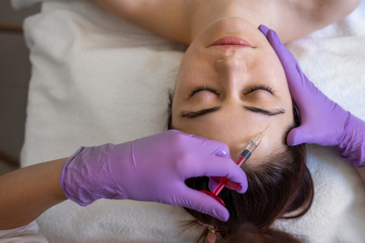 Provider injecting forehead, purple gloves, treatment bed